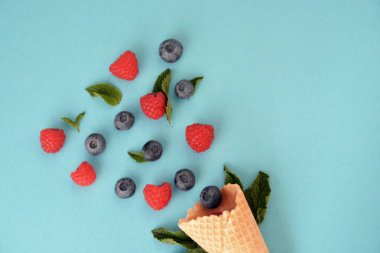 Ferahlatıcı bir yaz meyveli dondurma sembolü olarak renkli bir arka plan üzerinde yaban mersini, ahududu ve nane ile bir dondurma konisi