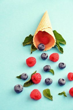 Ferahlatıcı bir yaz meyveli dondurma sembolü olarak renkli bir arka plan üzerinde yaban mersini, ahududu ve nane ile bir dondurma konisi