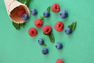 Ferahlatıcı bir yaz meyveli dondurma sembolü olarak renkli bir arka plan üzerinde yaban mersini, ahududu ve nane ile bir dondurma konisi