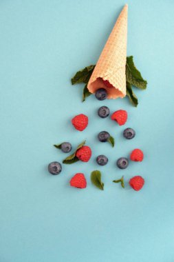 Ferahlatıcı bir yaz meyveli dondurma sembolü olarak renkli bir arka plan üzerinde yaban mersini, ahududu ve nane ile bir dondurma konisi