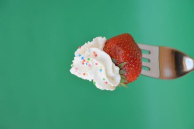 Renkli bir arka plan önünde krem ile bir çatal ucunda Çilek 