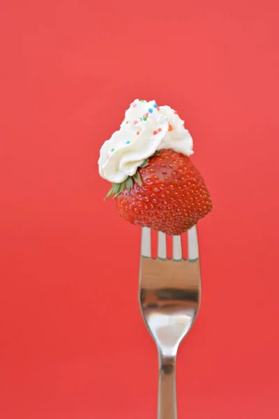 Strawberry on the tip of a fork with cream on it in front of a colorful background