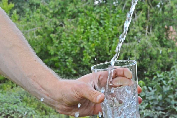 Свежая Чистая Вода Течет Стакане Перед Зеленым Летним Фоном Держится — стоковое фото