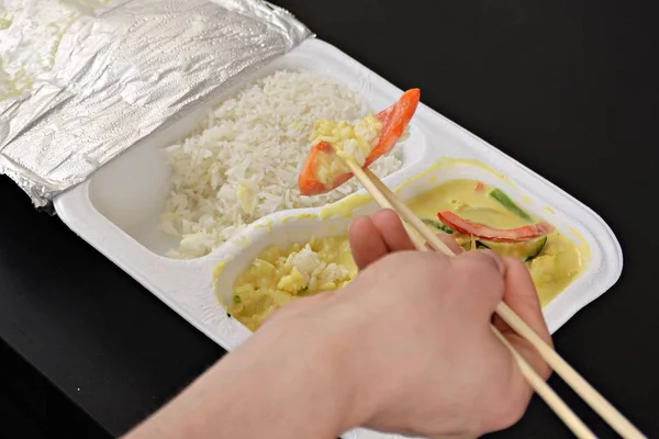 Close-up: eat yellow curry with rice from a styrofoam box with chopsticks