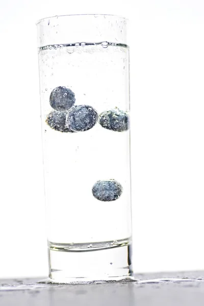 スパークリングウォーターでいっぱいのグラスにブルーベリーを落とす 隔離されたガラスの上に閉じる — ストック写真