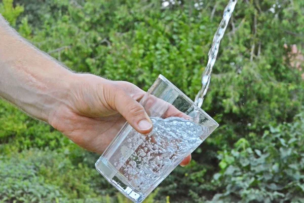 Świeża Czysta Woda Przepływa Szklance Przed Zielonym Letni Tło Trzymane — Zdjęcie stockowe