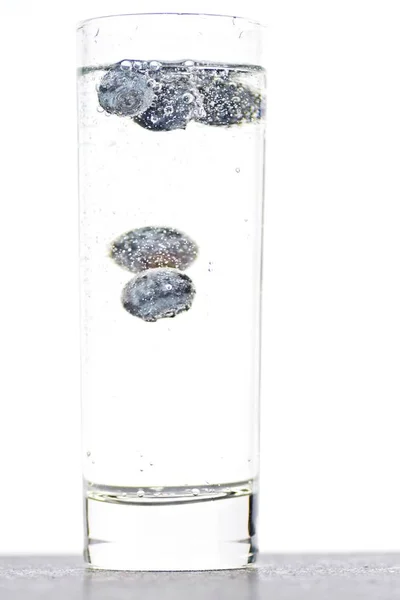 スパークリングウォーターでいっぱいのグラスにブルーベリーを落とす 隔離されたガラスの上に閉じる — ストック写真