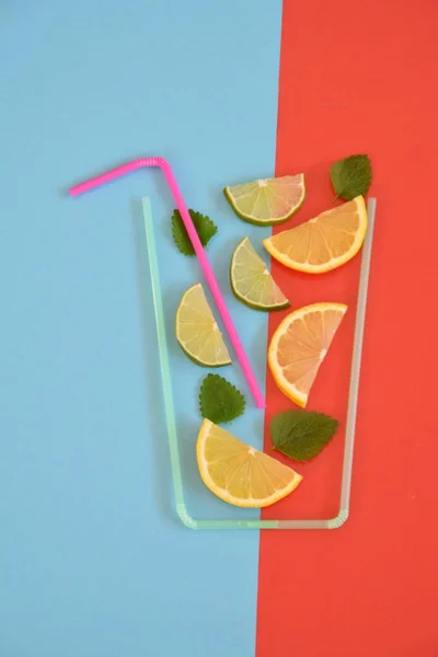 Creative layout strawberry lemonade ingredients - lemon, citrus, ice falling in glass made with cocktail straws on colorful background. Summer drinks. Minimal food concept. Selective focus.