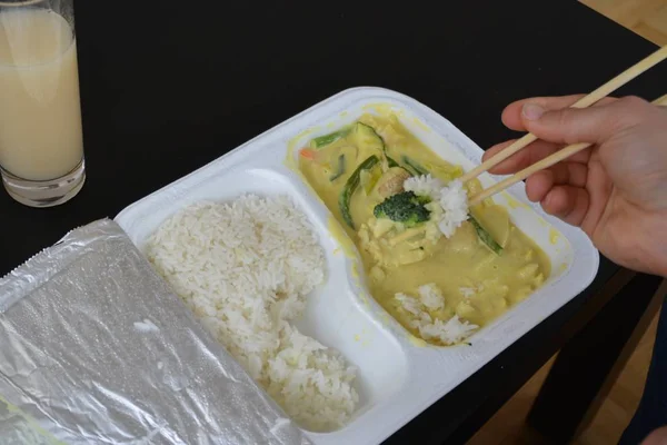 Close-up: eat yellow curry with rice from a styrofoam box with chopsticks