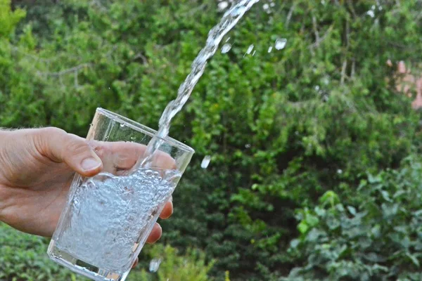 Świeża Czysta Woda Przepływa Szklance Przed Zielonym Letni Tło Trzymane — Zdjęcie stockowe