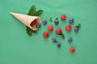 Ferahlatıcı bir yaz meyveli dondurma sembolü olarak renkli bir arka plan üzerinde yaban mersini, ahududu ve nane ile bir dondurma konisi