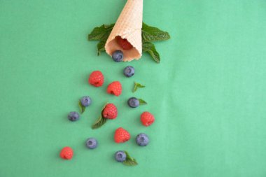 Ferahlatıcı bir yaz meyveli dondurma sembolü olarak renkli bir arka plan üzerinde yaban mersini, ahududu ve nane ile bir dondurma konisi