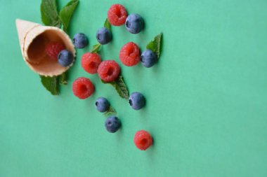 Ferahlatıcı bir yaz meyveli dondurma sembolü olarak renkli bir arka plan üzerinde yaban mersini, ahududu ve nane ile bir dondurma konisi