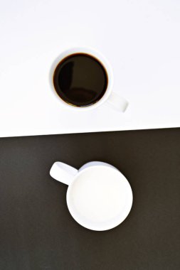 Yarım siyah ve yarım beyaz arka plan önünde iki bardak, bir fincan kahve içerir, diğer süt ve her ikisi de bir kontrast creat, kahve fincanları ile yin ve yang için kavram
