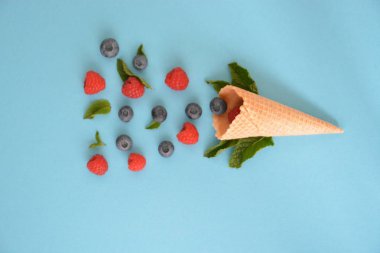 Ferahlatıcı bir yaz meyveli dondurma sembolü olarak renkli bir arka plan üzerinde yaban mersini, ahududu ve nane ile bir dondurma konisi