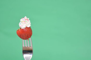 Renkli bir arka plan önünde krem ile bir çatal ucunda Çilek