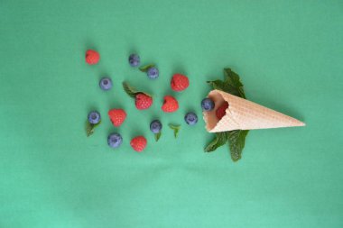 Ferahlatıcı bir yaz meyveli dondurma sembolü olarak renkli bir arka plan üzerinde yaban mersini, ahududu ve nane ile bir dondurma konisi