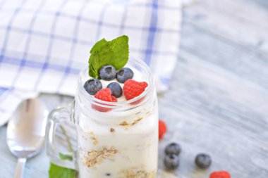 Yaz gününe iyi bir başlangıç için taze ve sağlıklı bir kahvaltı olarak yoğurt, yaban mersini ve ahududu ile yulaf ezmesi ve granola Cam