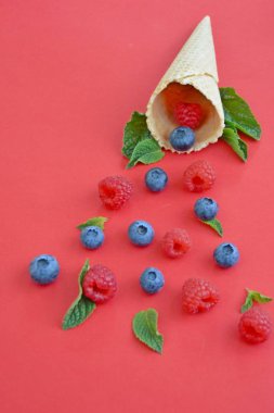 Ferahlatıcı bir yaz meyveli dondurma sembolü olarak renkli bir arka plan üzerinde yaban mersini, ahududu ve nane ile bir dondurma konisi