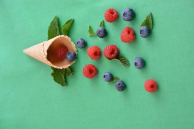 Ferahlatıcı bir yaz meyveli dondurma sembolü olarak renkli bir arka plan üzerinde yaban mersini, ahududu ve nane ile bir dondurma konisi