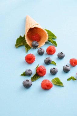 Ferahlatıcı bir yaz meyveli dondurma sembolü olarak renkli bir arka plan üzerinde yaban mersini, ahududu ve nane ile bir dondurma konisi