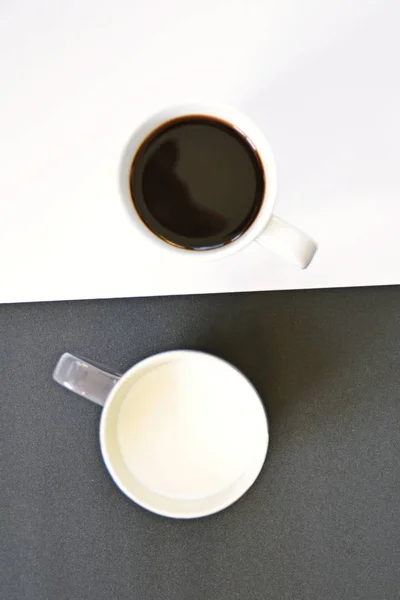 半分の黒と半分の白の背景の前に2つのカップは 一つのカップはコーヒー 他のミルクと両方がコントラストを含み コーヒーカップと陰と陽の概念が含まれています — ストック写真