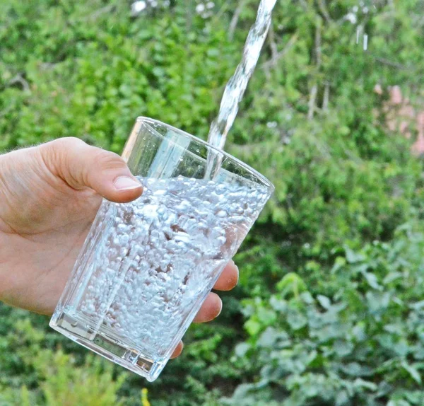 Свежая Чистая Вода Течет Стакане Перед Зеленым Летним Фоном Держится — стоковое фото