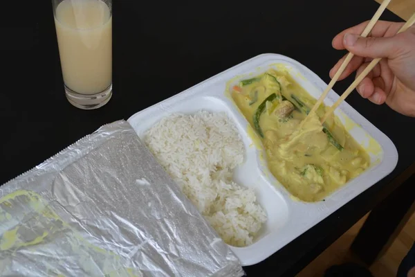 Close-up: eat yellow curry with rice from a styrofoam box with chopsticks