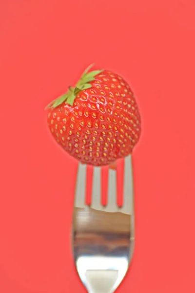 Strawberry on the tip of a fork in front of a colorful background