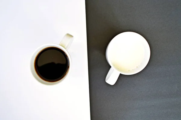 半分の黒と半分の白の背景の前に2つのカップは 一つのカップはコーヒー 他のミルクと両方がコントラストを含み コーヒーカップと陰と陽の概念が含まれています — ストック写真