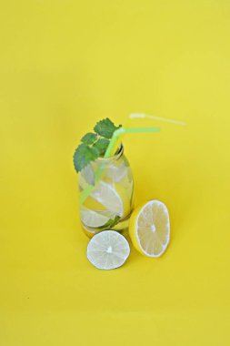 Düz bir arka plan karşı yaz aylarında meyveli bir ferahlık olarak su dolu bir şişe limon, nane ve limon parçaları