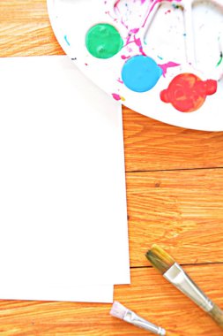 Bir renk paleti ve birçok fırça lar yanı sıra ahşap bir arka plan üzerinde fırça su renkleri ile bir kağıt levha