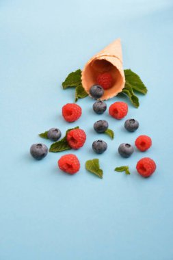 Ferahlatıcı bir yaz meyveli dondurma sembolü olarak renkli bir arka plan üzerinde yaban mersini, ahududu ve nane ile bir dondurma konisi