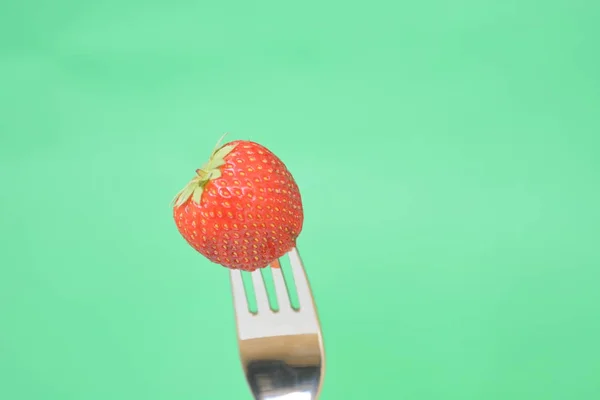 Strawberry on the tip of a fork in front of a colorful background