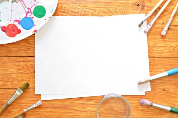 Bir renk paleti ve birçok fırça lar yanı sıra ahşap bir arka plan üzerinde fırça su renkleri ile bir kağıt levha