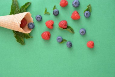 Ferahlatıcı bir yaz meyveli dondurma sembolü olarak renkli bir arka plan üzerinde yaban mersini, ahududu ve nane ile bir dondurma konisi