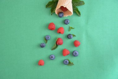 Ferahlatıcı bir yaz meyveli dondurma sembolü olarak renkli bir arka plan üzerinde yaban mersini, ahududu ve nane ile bir dondurma konisi