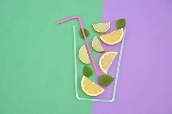 Creative layout strawberry lemonade ingredients - lemon, citrus, ice falling in glass made with cocktail straws on colorful background. Summer drinks. Minimal food concept. Selective focus.