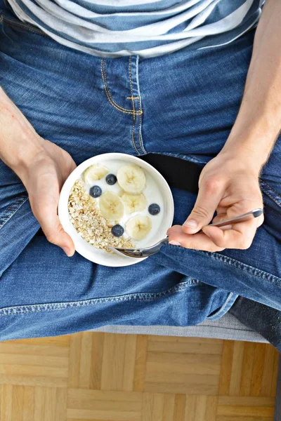 close up - man eat healthy breakfast with oatmeal, bananas, blueberries and yoghurt