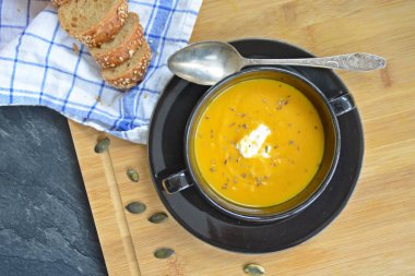 Küçük bir kapta kabak krema çorbası ve yanında bütün bir kabak ve dilimlenmiş ekmek ile mutfak yüzeyinde ahşap bir tahta üzerinde - sonbahar şölen 