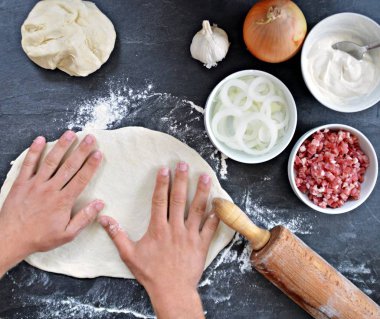 Yakın çekim-adam siyah mutfak yüzeyinde bir Alsas tarte pasta için hamur dışarı rulo-yanında tarte flambe için maddeler vardır