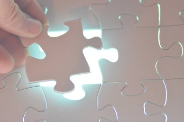 Yakın çekim bir el Toplam bulmaca beyaz bir puzzle parçası koyarak. Eksik parçanın yüzeyi parlak parlar-tamamlanmış bir projenin radyant başarısının sunumu için konsept 
