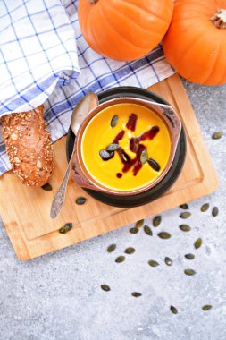 Küçük bir kapta kabak krema çorbası ve yanında bütün bir kabak ve dilimlenmiş ekmek ile mutfak yüzeyinde ahşap bir tahta üzerinde - sonbahar şölen 