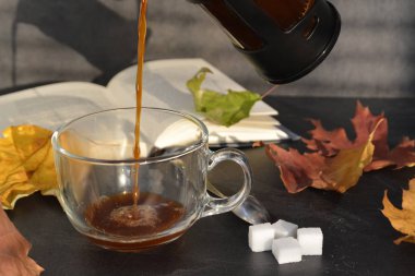 Bir cam fincan içine bir sonbahar ayarı kahve dökün-bir cam fincan kuru ve renkli sonbahar yaprakları ve arka planda bir kitap yanında standig ve birisi içine kahve dökme olduğunu