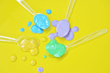Düz bir arka planda boya farklı damla ile şeffaf kaşıklar-metin alanı ile arka plan olarak renk ile plastik kaşık 