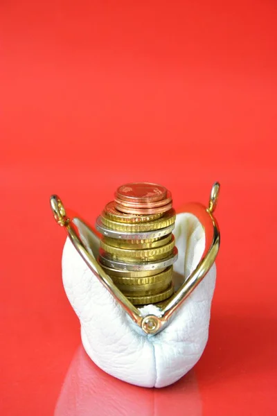 An old white purse with euro coins topped on each other in it in front of a red background with space for text and other elements - konzept for poverty in the age with focus on the coins