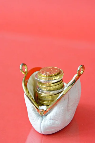 An old white purse with euro coins topped on each other in it in front of a red background with space for text and other elements - konzept for poverty in the age with focus on the coins