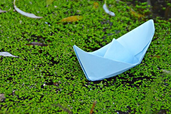 A self-folded paper boat floats on the ground in autumn in a puddle accumulated by the rain