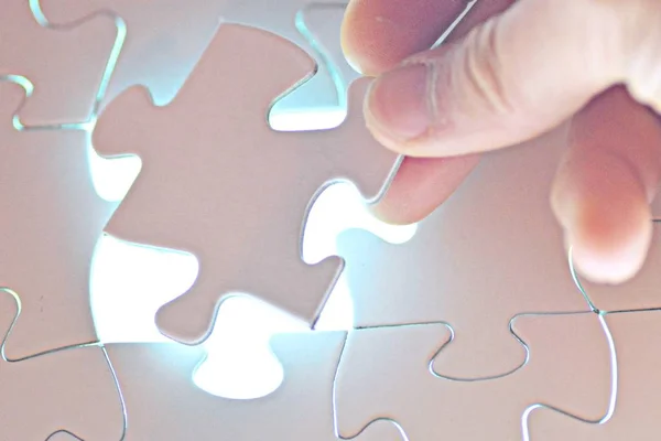 Close-up of a hand putting a white puzzle piece in a total puzzle. The surface of the missing part shines brightly - Concept for the presentation of the radiant success of a completed project