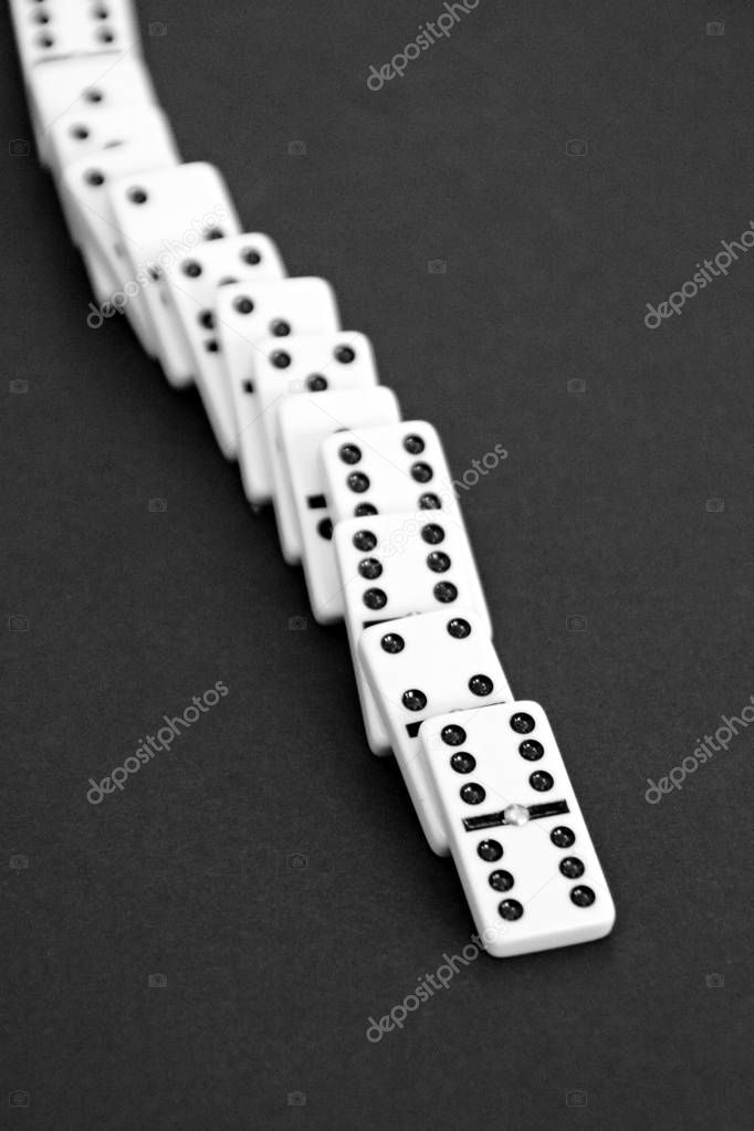 Bright dominoes against a black background with shallow depth of field as a concept for business concepts and subsequent reactions of individual decisions and individual actions